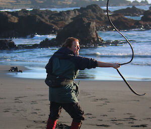 A woman standing out the beach waving some rope around.