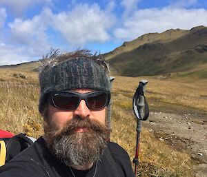 A man walking out on a trail with lots of vegetation and hills.