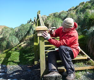 Man outdoors wearing a red raincoat and using tools to fix wooden staircase