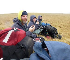 Three people sitting in a field eating.