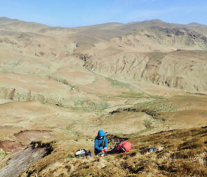 Girl wearing a blue jacket with a red backpack on the ground working on a hill.