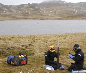 A historical photograph showing field assistants describing the core at Emerald Lake, Macquarie Island