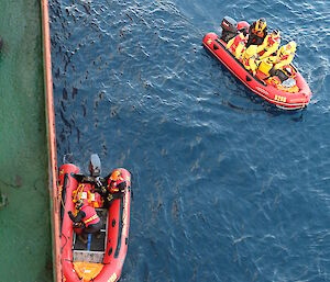 Two inflatable rubber boats beside the RV Aurora Australis off shore at Macquarie Island. One is loaded with several passengers ready to be ferried to the shore