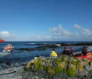 An AAD LARC in the surf off Landing Beach, Macquarie Island heading towards the RV Aurora Australis. In the foreground some expeditioners are watching beside two Inflatable Rubber Boats