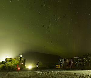 A green aurora in the background on a dark night with the station lit up in the foreground at Macca this week