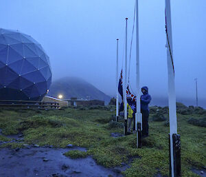 Two raincoat wearing epeditioners raise the NZ and Australian flags at dawn (0632) on the isthmus Macquarie Island