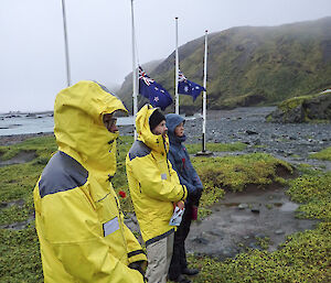 Raincoat clad expeditioners with flags at halfmast in the background at this weeks Anzac Day service on Macquarie Island