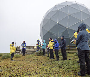 The expeditioners of the 71st ANARE congregate for the ANZAC day service in front of the flagpoles on the isthmus at Macquarie Island