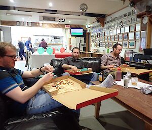 Angus Cummings, Greg Sandrey and Jeremy Bird sitting on the sofas in the mess at Macca eating pizzas from boxes for Jeremy Bird’s birthday