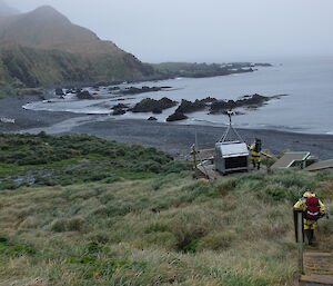 An expeditioner turns on the power supply (solar and wind generated) at Green Gorge as another expeditioner makes a beeline for the hut.