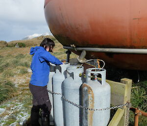 An expeditioner opens the gas bottles at Waterfall Bay Hut.