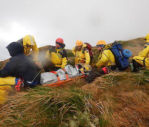 A team of rescuers get ready to lift Angus in the stretcher to carry him along a flatter section of hill in the recent Macca SAR exercise