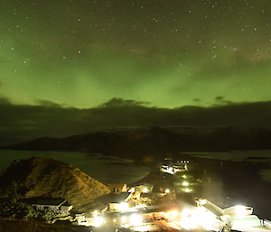 An image in the sequence of the time lapse showing a strong aurora in the sky over Macca with the lit station in the foreground