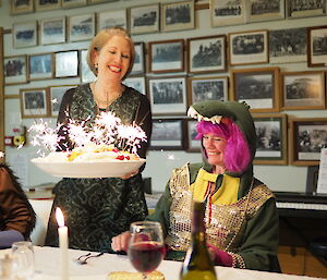 A pavlova with sparklers lit on top is delivered to Danielle at the table