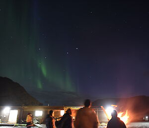 Expeditioners watching the aurora in the sky around a bonfire in a drum