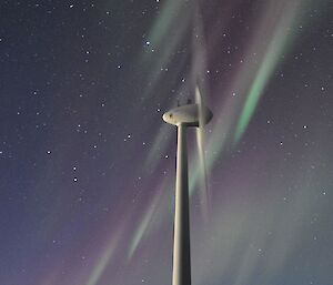 The Aurora is seen over the upper wind turbine on top of the hill