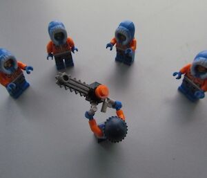 Lego men being trained in the use of a chainsaw