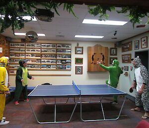 Expeditioners dressed as a tiger and dinosaur play ping pong against expeditioners dressed as a zebra and frog