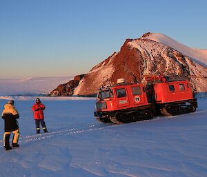 Two expeditioners stand near a large, tracked over-snow vehicle