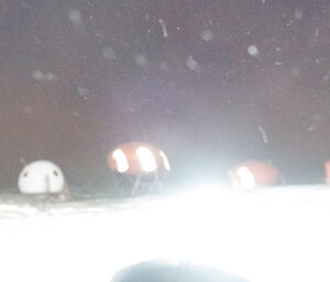 A camera flash illuminates snow and ice to create a bright light in front of melon shaped huts