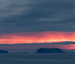 The horizon is glowing with orange to the north of Bechervaise Island over two massive icebergs
