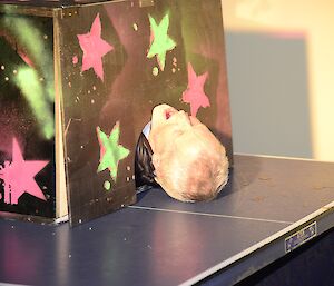 Male expeditioner in a fake magician’s box, where it appears that he has been sawn in half.