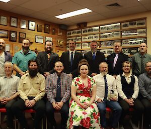 The Mawson 68th ANARE pose for a group photo. They are all dressed up, with the sole female in the middle wearing a beautiful dress.