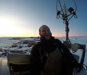 Male expeditioner laughing while half out of the top of the Mawson wind turbine.