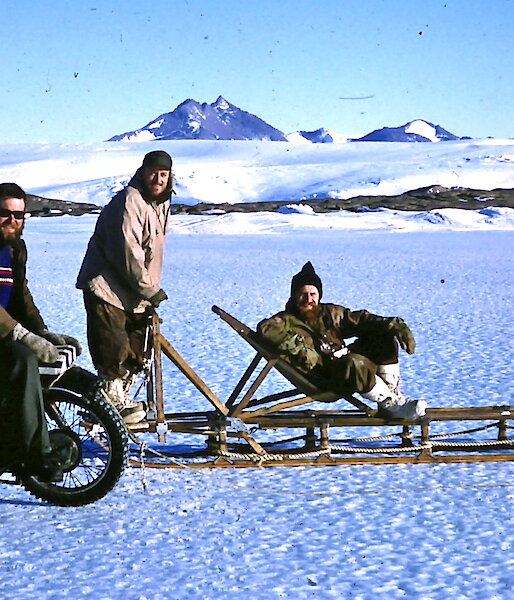 A Velocette motorcycle parked on the sea ice next to a dogsled and three men in 1960 near Mawson station.