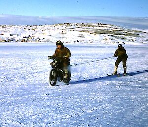 Velocette motorcycle towing a skier on sea ice at Mawson in 1960.