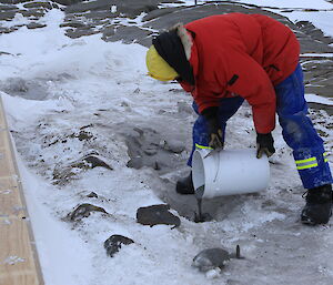 An expeditioner pours concrete into icy holes, to form anchors for the new hut.