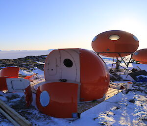 Sun shines on a half assembled hut while a taller and shorter hut are in the background complete.