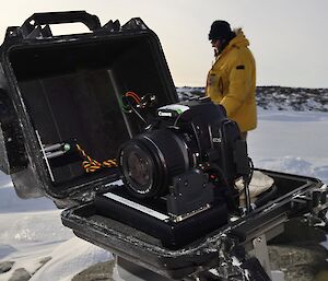 A camera is contained in a box with a lens cover which opens when a photo is to be taken. Expeditioner is seen in background.