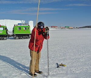 Kim drilling the sea ice with the Hägglunds and the station in the background.