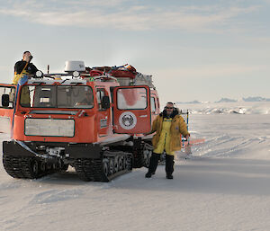 Two men near a Hägglunds over-snow vehicle.