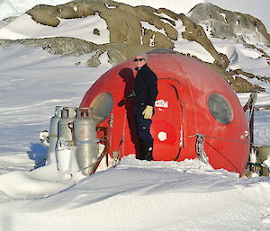 Angus in front of the red apple hut with an iceberg in the background..