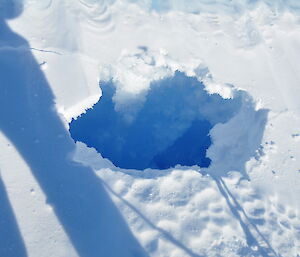 A hole in snow shows a deep crevasse below the ice