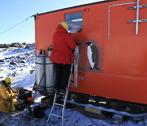 The station carpenter on a ladder replacing a cracked window pane at Colbeck hut.