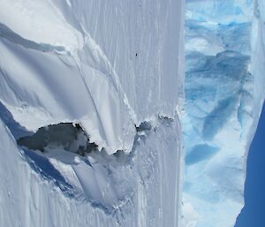 A very wide and deep crack with an ice berg in the back ground.