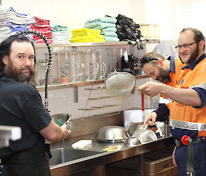 A couple of expert slushies at the sink with a load of dishes providing advice on how to clean them.