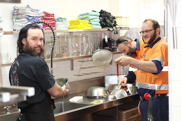 A couple of expert slushies at the sink with a load of dishes providing advice on how to clean them.