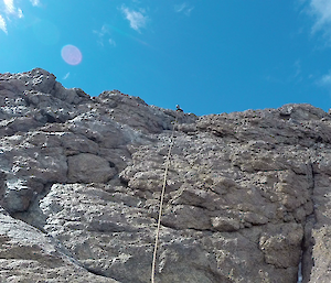 A cliff side with an expeditioner at top and climbing rope dangling below him.