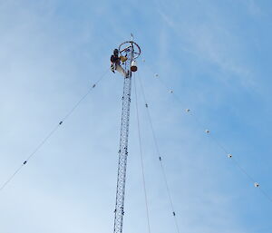 A tall pole with tethers with a man at the top working