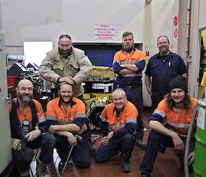 A group of male tradesmen pose for a photo inside the main power house surrounded by equipment
