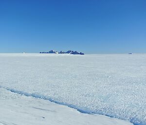 Rocky peaks visible in distance on otherwise flat, white, icy plateau