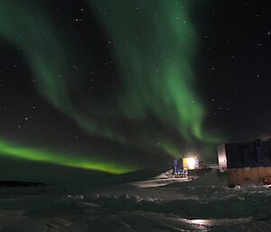 The green lights of an auroa spread across the sky above Mawson station