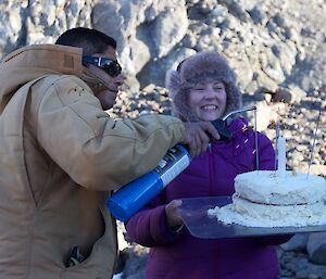 Male expeditioner lights sparklers on a cake with a blow torch