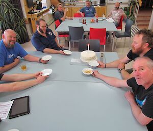 Expeditioners seated around the cake waiting to be served but their is no birthday girl to cut the cake.