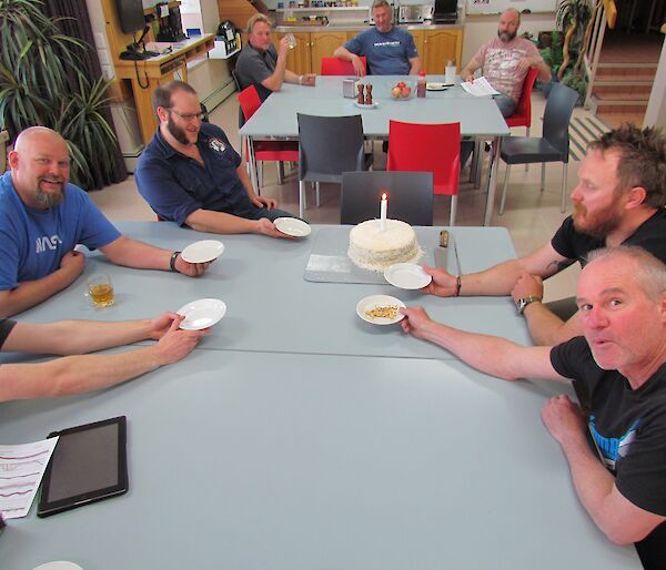 Expeditioners seated around the cake waiting to be served but their is no birthday girl to cut the cake.