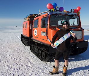 An expeditioner poses in front of a Hägglunds oversnow vehicle which is decorated with balloons
